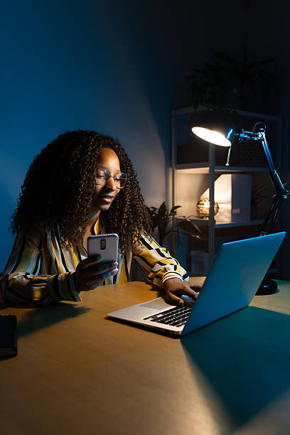istock Young woman working late at night using laptop and smartphone 2214871145