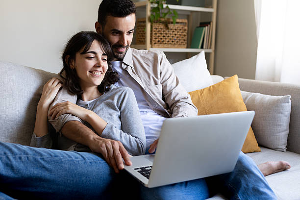 istock Happy couple relaxing on sofa browsing internet on laptop 2214871149