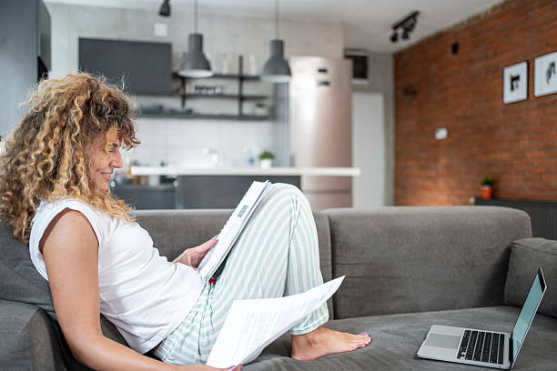istock Woman reviewing documents on sofa with laptop nearby 2214871434