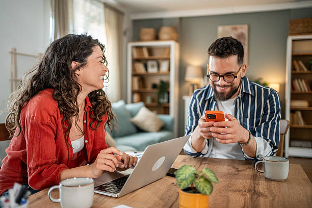 istock Young couple working from home, using laptop and smartphone, smiling and enjoying their time together 2214872453