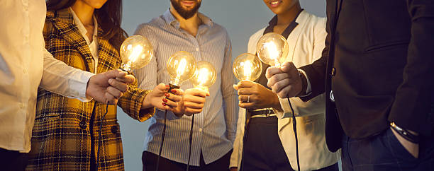 istock Multiethnic business team joining glowing light bulbs as metaphor for teamwork and sharing ideas 2214881642