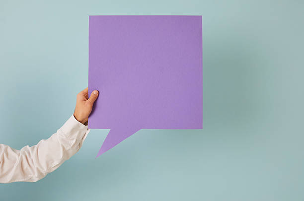 Anonymous adult male holding in hand one square shaped purple mockup copyspace speech bubble on blue background. Man showing violet message balloon with free, blank, clean space for expressing opinion