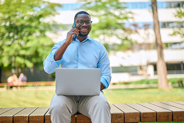 istock Businessman working with laptop and talking on smartphone in a park 2214889223
