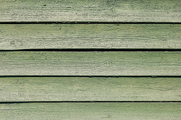 Close-up view of weathered green wooden planks showing natural grain and texture under sunlight. The surface reveals age and character.