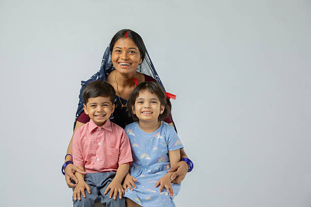 Three rural Indian children sit on a low barrier in a lush green cornfield, playfully posing with the gestures of see no evil, speak no evil, and hear no evil. The cheerful scene reflects innocence, unity, and rural childhood fun.