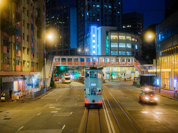 A double-decker tram glides through Causeway Bay at night. The street is busy with  glowing signage. Hong Kong
