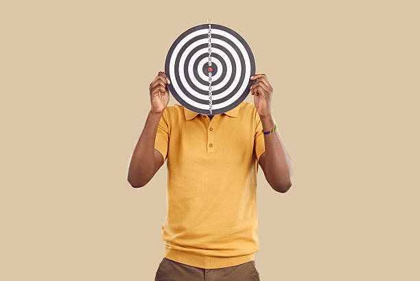 istock Unknown ethnic man covers his face with darts board, which symbolizes achievement of goals. 2214901569