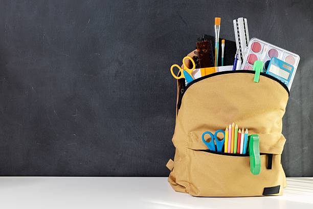 istock School backpack full of Stationery Supplies on blackboard with copy space 2214902285