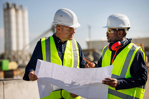 istock Two construction engineers discussing blueprints at an industrial site 2214904835