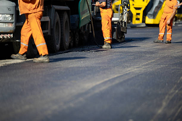 istock Road construction crew works on asphalt paving at a traffic site in bright orange uniforms 2214905384