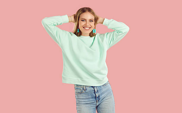 istock Happy, smiling young woman, dressed in light mint sweater and blue jeans, dances and throws her hands behind her head. 2214910110