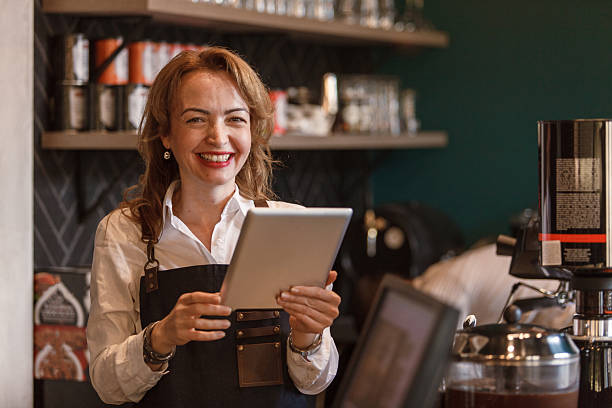 istock Friendly barista smiling and using a digital tablet in a modern cafe 2214910989