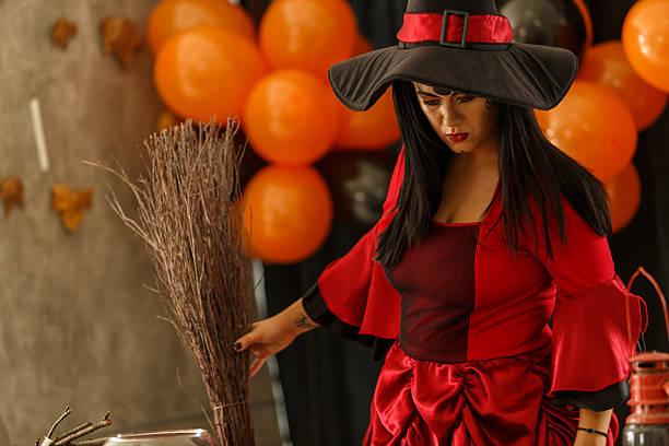 A woman dressed as a witch in red and black prepares Halloween decorations with themed colors.