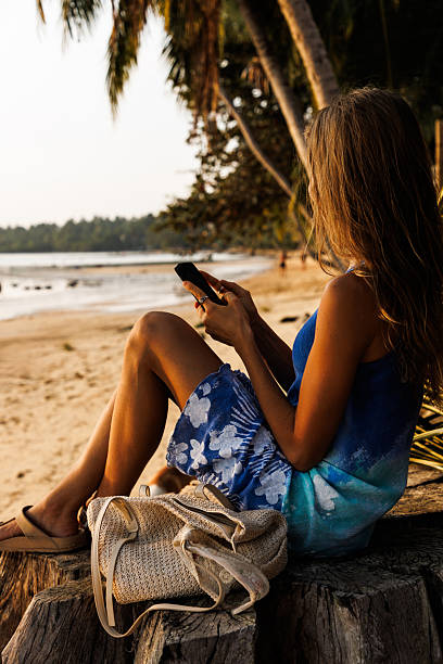 istock Woman relaxing on a tropical beach using a phone, with palm trees and sunset 2214916333