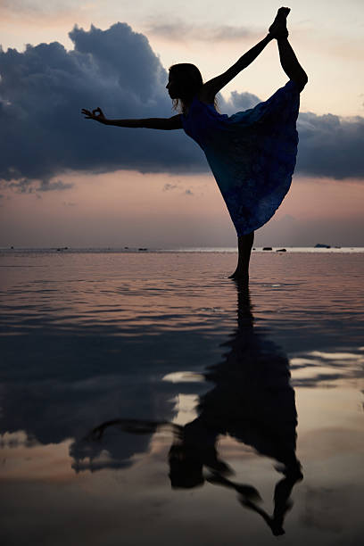 The silhouette of a woman with long hair against the background of the setting sun over the sea.