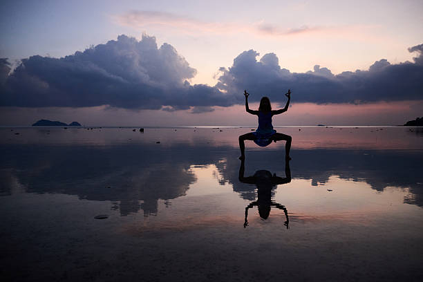 istock Silhouette of a person meditating by a reflective beach during sunset 2214918302