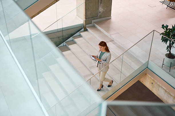 istock Businesswoman walking down the stairs in modern office building using digital tablet 2214925833