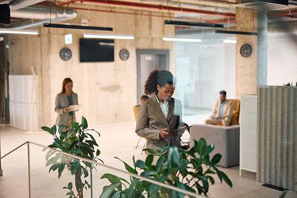 istock Businesswoman using digital tablet in modern office lobby with colleagues working 2214926122