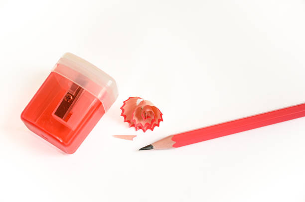 Red pencil sharpener with colorful wood shavings and red pencil on white background. Ideal for education, stationery, school supplies, and creative learning materials.