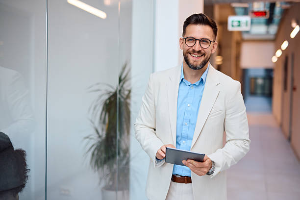 istock Businessman smiling and using digital tablet in office hallway 2214928458