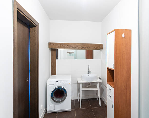 istock Modern Home Bathroom Interior Featuring Sink, Washing Machine, and Wooden Cabinets 2214929306