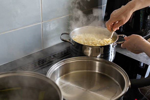 A person is energetically stirring pasta on the stovetop, enveloped by steam and bubbling boiling water