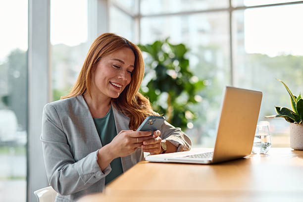 istock Smiling businesswoman using smartphone and laptop in modern office 2214929876