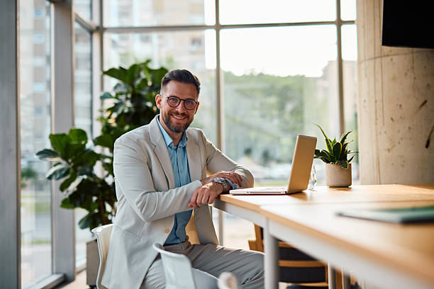 Businessman smiling and looking at camera while working on laptop in office