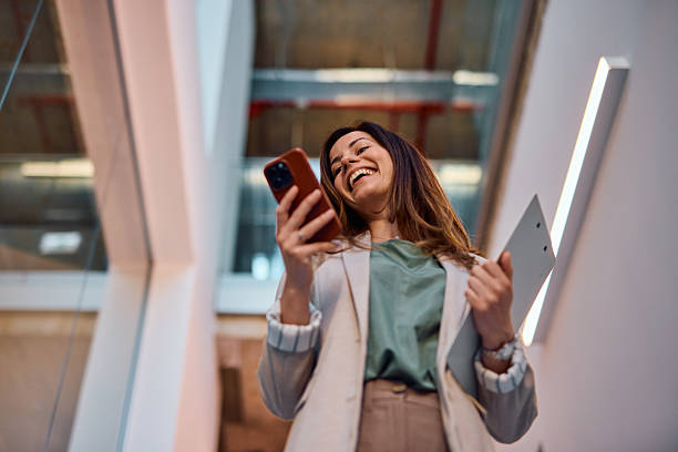 istock Businesswoman laughing while reading a message on her phone in a modern office 2214939541