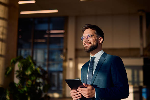 Smiling businessman holding tablet and looking up in office lobby