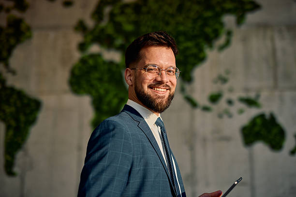 istock Smiling businessman holding tablet with world map in background 2214941410