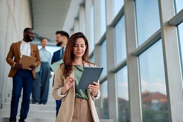 istock Businesswoman using digital tablet while walking in office hallway with colleagues 2214941432