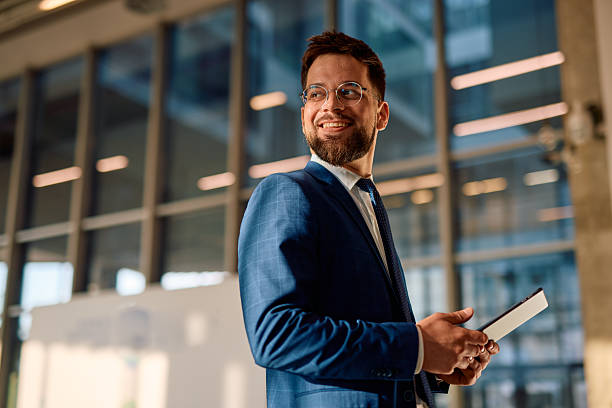 istock Businessman smiling and holding a tablet looking away in modern office 2214941737