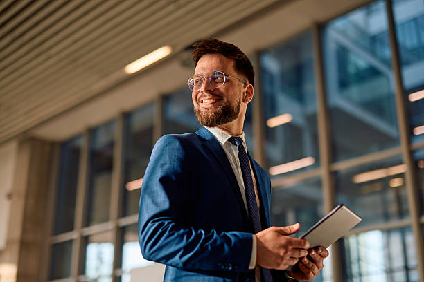 istock Smiling businessman holding tablet and looking away in modern office 2214941738