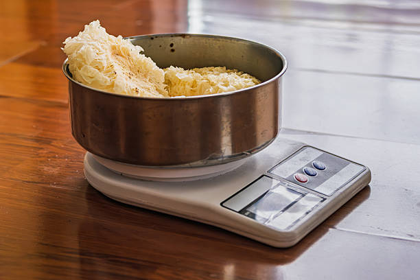 Close-up of a stainless steel bowl filled with snow white fungus being weighed on a digital kitchen scale on a wooden table.