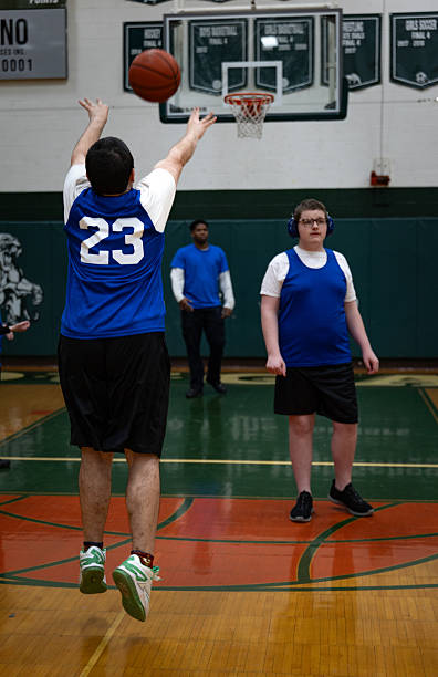 A waist-up shot of a young Asian female basketball player holding a ball and shooting on an indoor court during training.