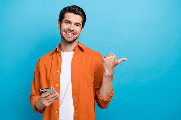 istock Photo of positive guy beaming smile hold use iphone apple gadget direct finger empty space isolated on blue color background 2214949937