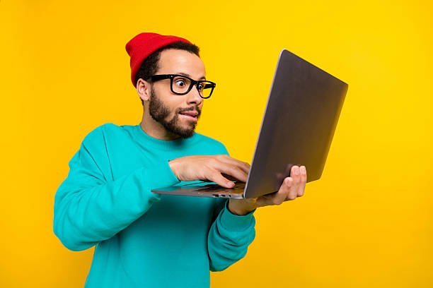 istock Portrait of astonished excited man with beard dressed turquoise pullover look at laptop typing email isolated on yellow color background 2214950542