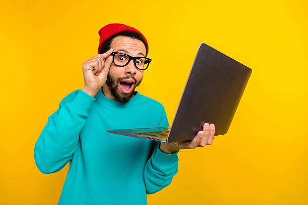 istock Portrait of impressed man with beard dressed turquoise pullover hold laptop touch eyewear staring isolated on yellow color background 2214950851