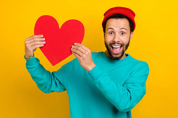 istock Portrait of ecstatic overjoyed man with beard dressed turquoise pullover demonstrate large paper heart isolated on yellow color background 2214950889