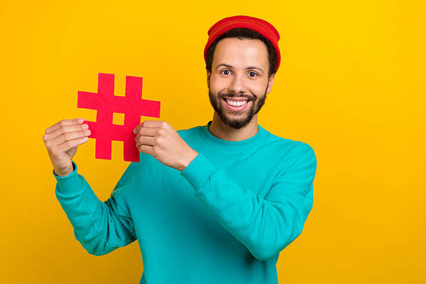 istock Portrait of toothy beaming cheerful man with beard dressed turquoise pullover fingers holding hashtag isolated on yellow color background 2214951015