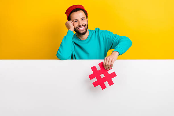 istock Portrait of funny man with beard dressed turquoise pullover hold hashtag lean on poster empty space isolated on yellow color background 2214951057