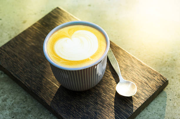 Hot latte coffee cup with spoon and wooden plate on table.