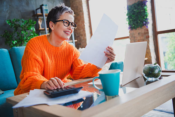 istock Photo of charming positive elderly lady wear orange pullover counting records modern device indoors apartment room 2214951616