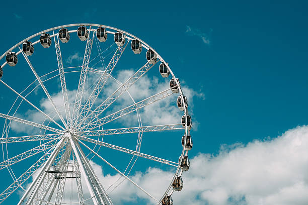 istock A towering Ferris wheel stands against a bright blue sky with fluffy white clouds in a vibrant amusement park setting during the day 2214952665