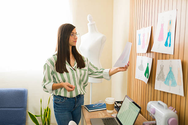 istock Clothing designer comparing dress sketches and choosing fabrics in her workshop 2214953968
