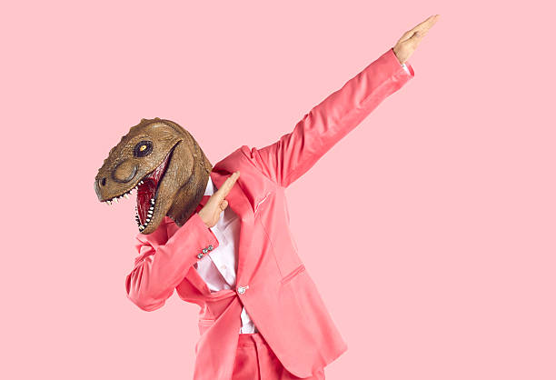 istock Cheerful young man in dinosaur rubber mask makes dab dance gesture isolated on pink background. 2214968694