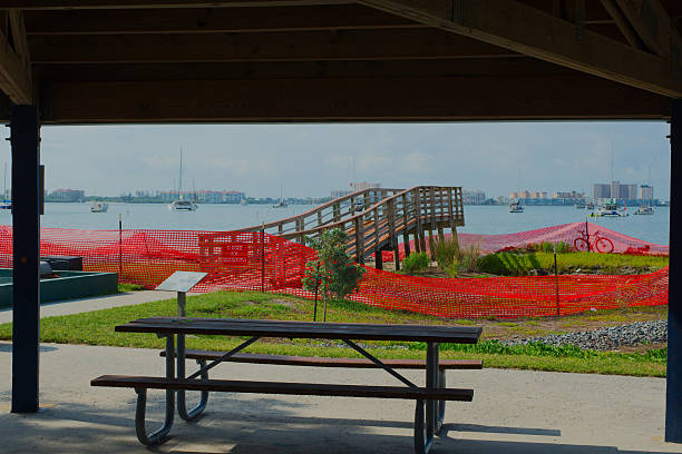 Serene Waterfront Scene with Pier, Boats, and Undercover Picnic Setting. Gulfport, Florida. Framed Picturesque waterfront view with boats anchored in the harbor, a wooden pier extending into the water, from a picnic table sheltered by a wooden structure, offering a tranquil and relaxing atmosphere. gulfport florida photos stock pictures, royalty-free photos & images