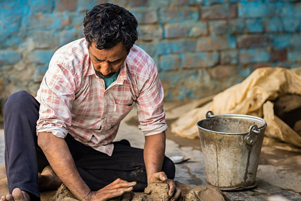 Professional Indian potter man kneading clay and preparing it for making mud pots on a pottery wheel at his workshop.