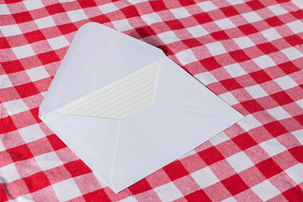 Open white envelope with blank lined card inside, on red checkered tablecloth background, perfect for adding messages, invitations, or greetings